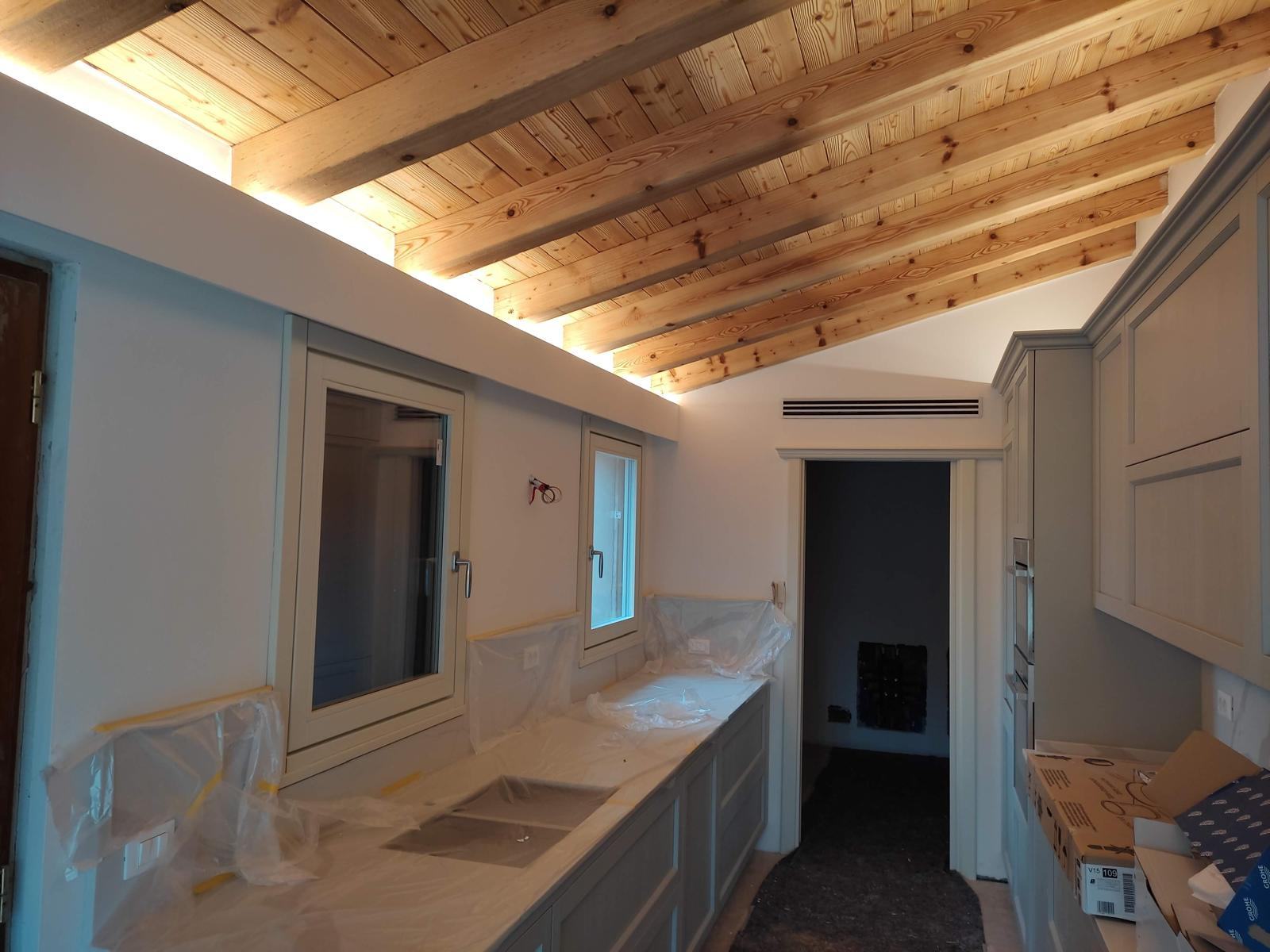 Cucina con travi in legno a vista e illuminazione lineare sul soffitto.