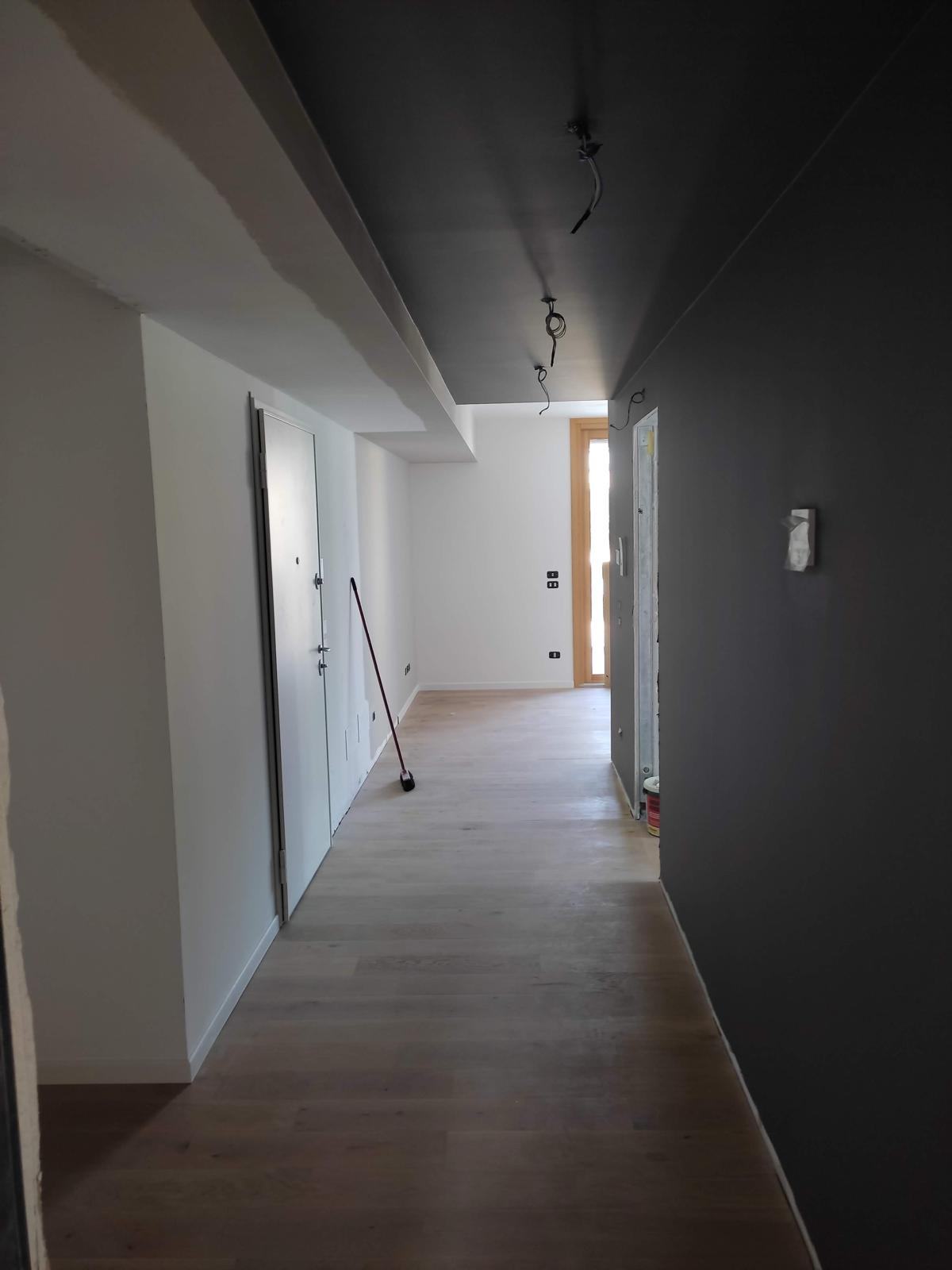 Ingresso con parete grafite, pavimento chiaro e punti luce a soffitto.